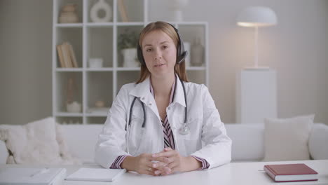 Junge-Ärztin-Berät-Online,-Schaut-In-Die-Kamera-Und-Spricht-über-Kopfhörer-Mit-Mikrofon.-Ärztin-Arbeitet-Aus-Der-Ferne